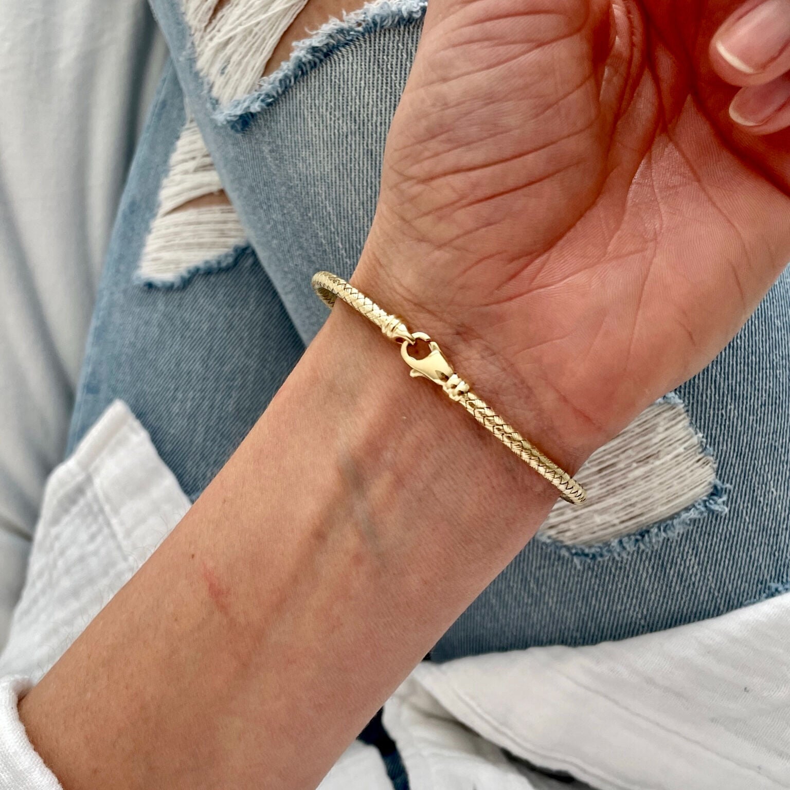 14K yellow gold woven bangle bracelet paired with ripped blue jeans and a white top, giving the look effortless elegance. Perfect for everyday wear or weekend outings.