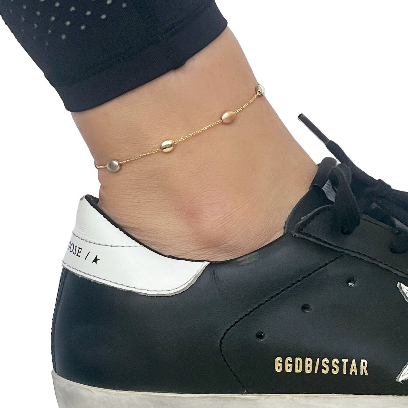 14k tricolor pebble bead station anklet, polished and satin beads on a yellow gold chain, secured with lobster clasp, on a model's ankle