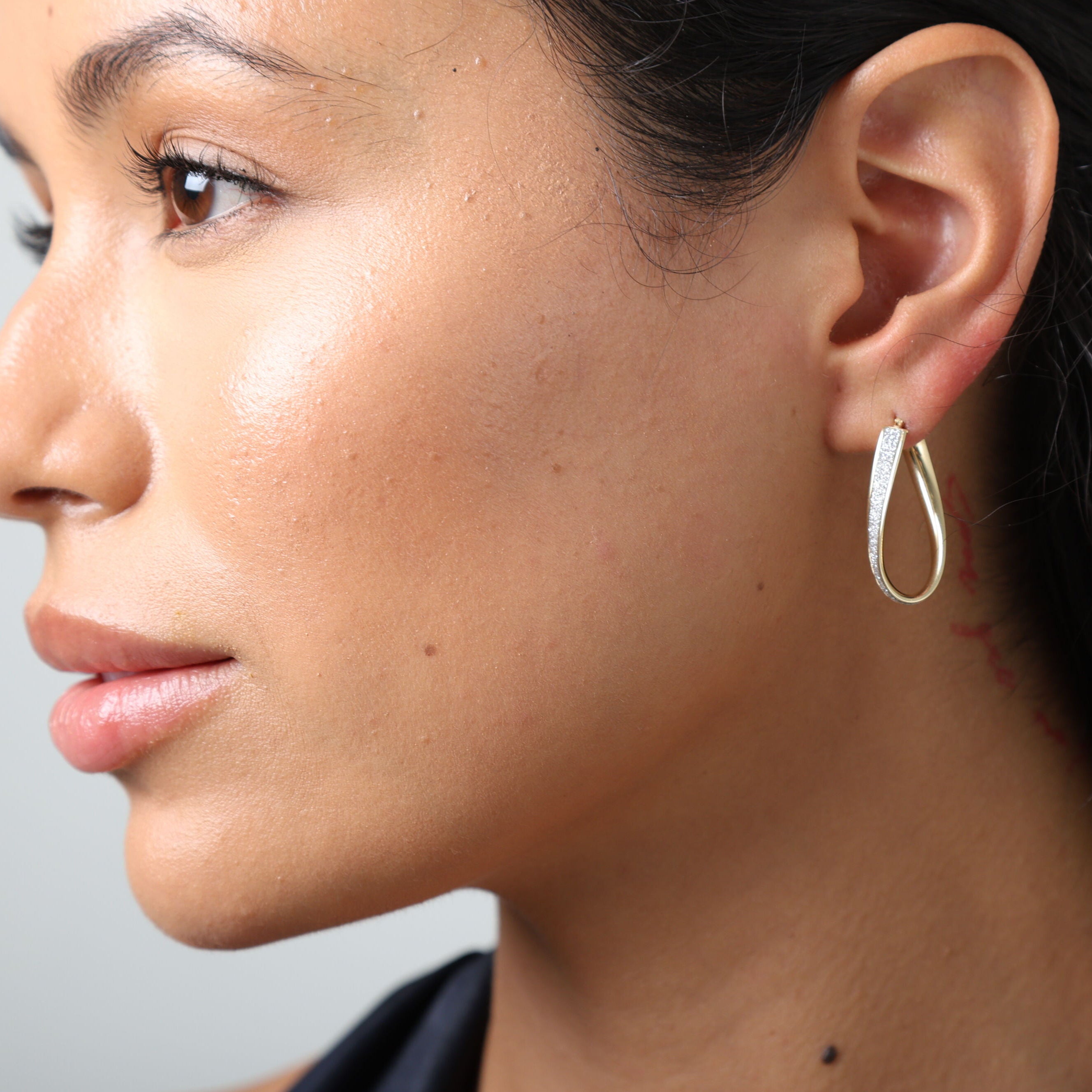 Close-up of a woman wearing a gold hoop earring against a neutral background
