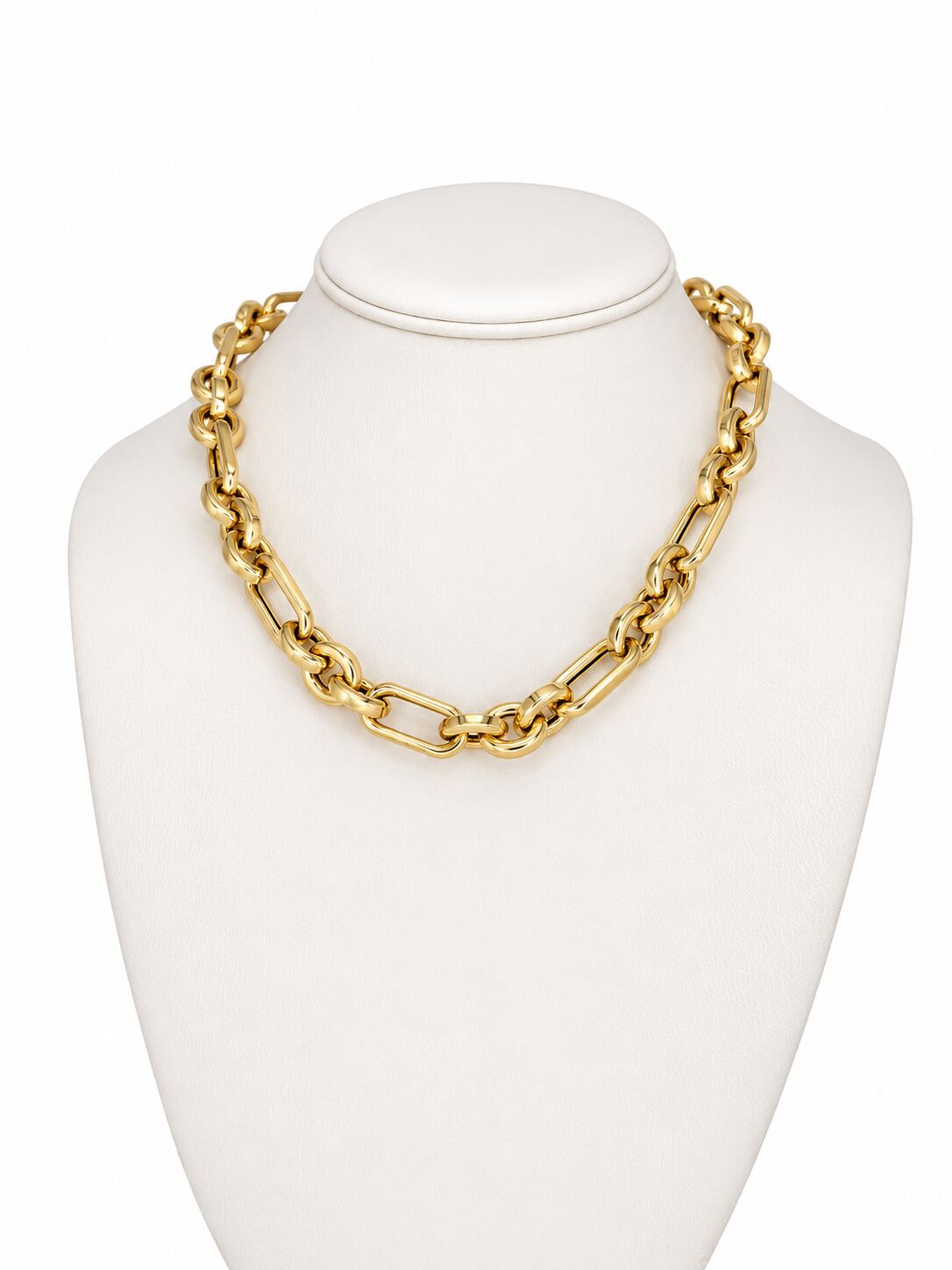 A chunky gold chain necklace with alternating round and elongated links, displayed on a white jewelry bust against a white background.