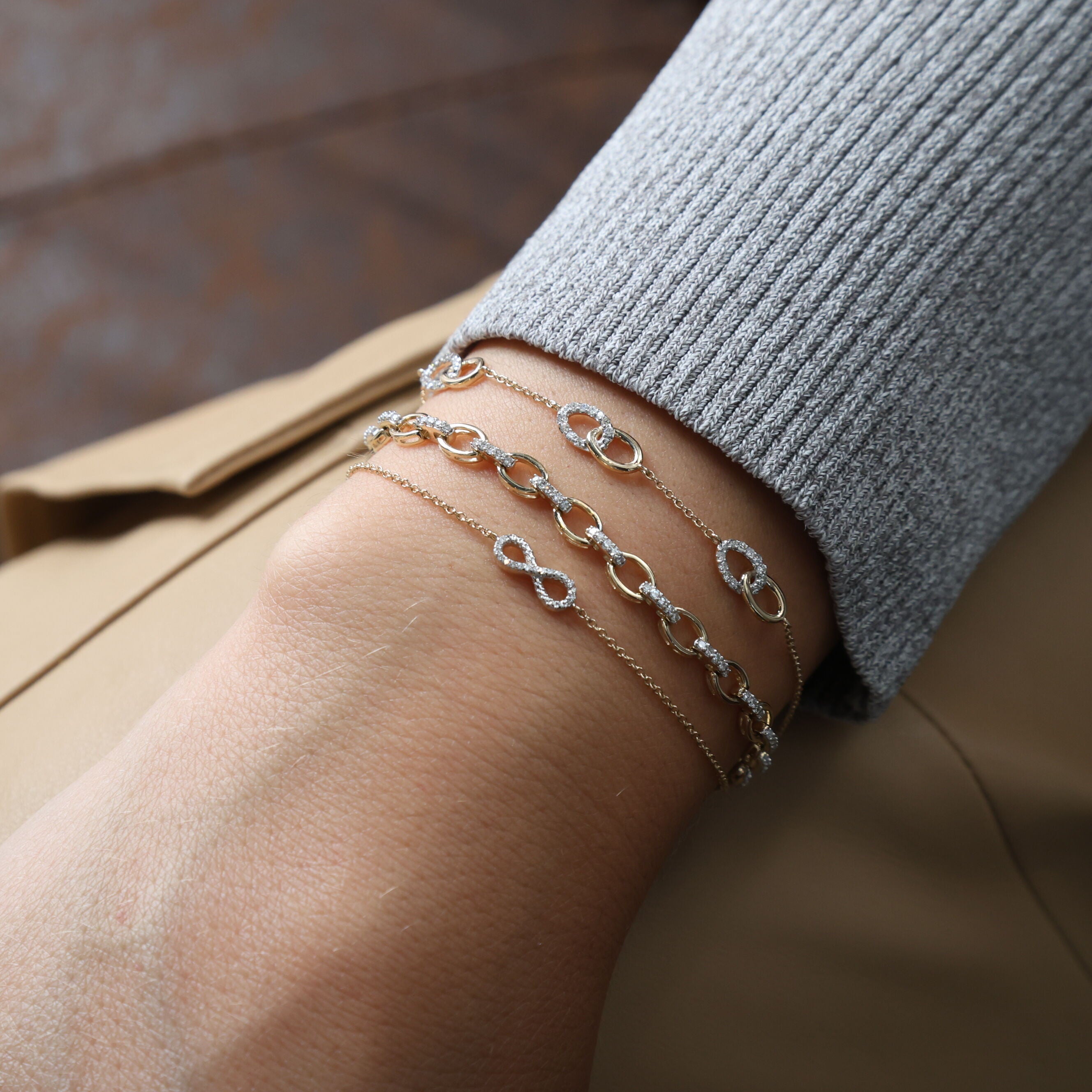 Diamond Oval Link Chain Bracelet in 14K Yellow Gold styled with stacked rings and layered necklaces over a soft grey sweater. The bracelet’s brilliance enhances the look with effortless sophistication, perfect for milestone celebrations, weddings, or polished office style.