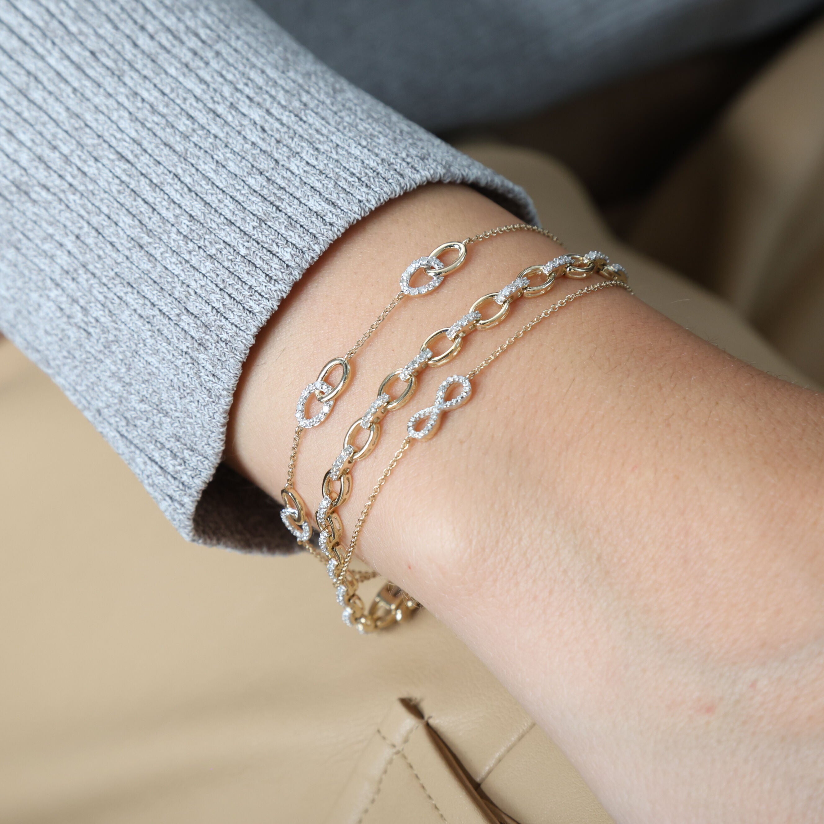 Diamond Oval Link Chain Bracelet in 14K Yellow Gold styled on the wrist with layered diamond bracelets and a grey knit sleeve. The sparkling oval links add confidence and sophistication, perfect for workdays, casual meetups, or effortless everyday elegance.