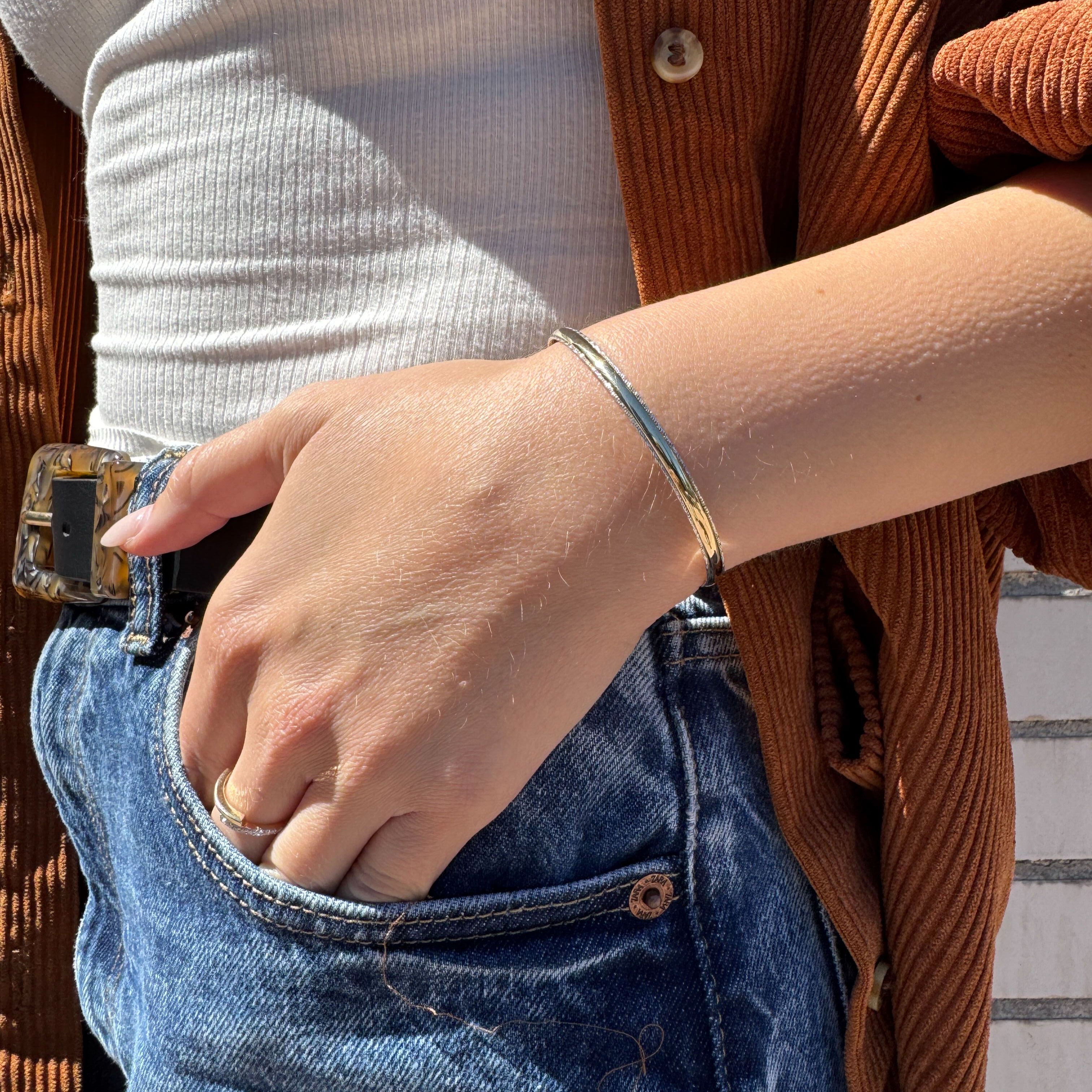 14K two-tone glitter edge gold bangle bracelet styled on the wrist with high-waisted denim jeans, creating a relaxed yet polished look. Ideal for casual Fridays, daytime strolls, and effortless everyday wear.