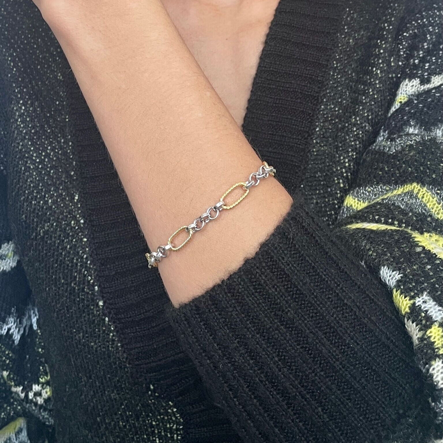 14K two tone gold bracelet with oval and round links styled on the wrist with a cozy black knit sweater. The polished contrast of yellow and white gold enhances the outfit with sophistication and timeless appeal. Ideal for casual meetings, weekend outings, or workday elegance.