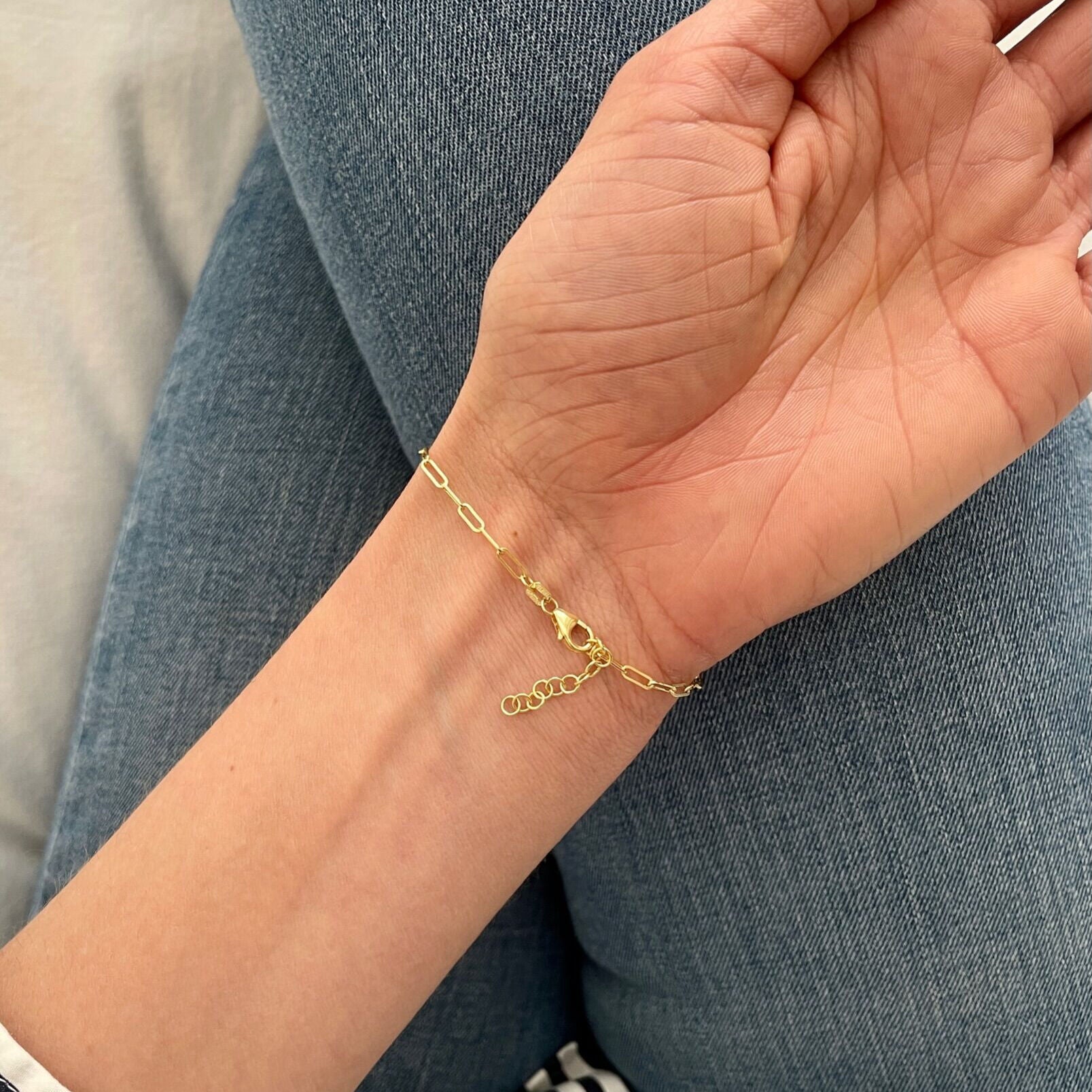 14K Gold Paperclip ID Bar Bracelet worn on wrist, paired with a relaxed striped sleeve for a chic casual style.