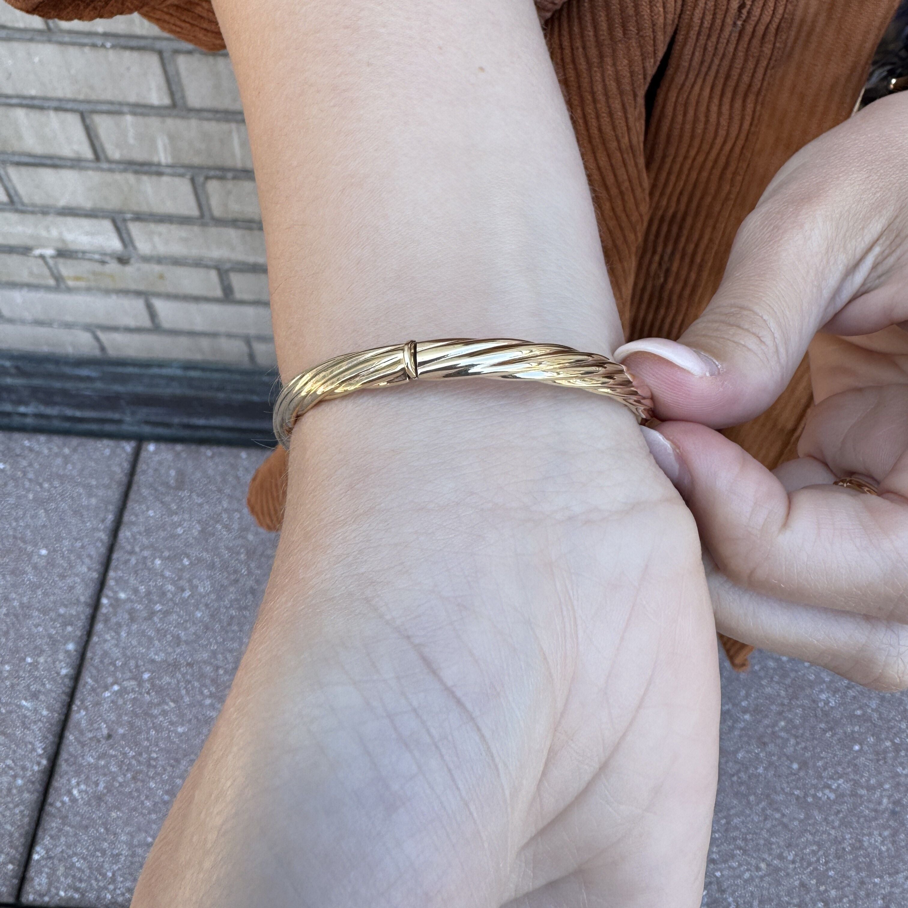 Close-up shot of the twisted gold bangle on wrist showing the clasp and intricate woven texture.
