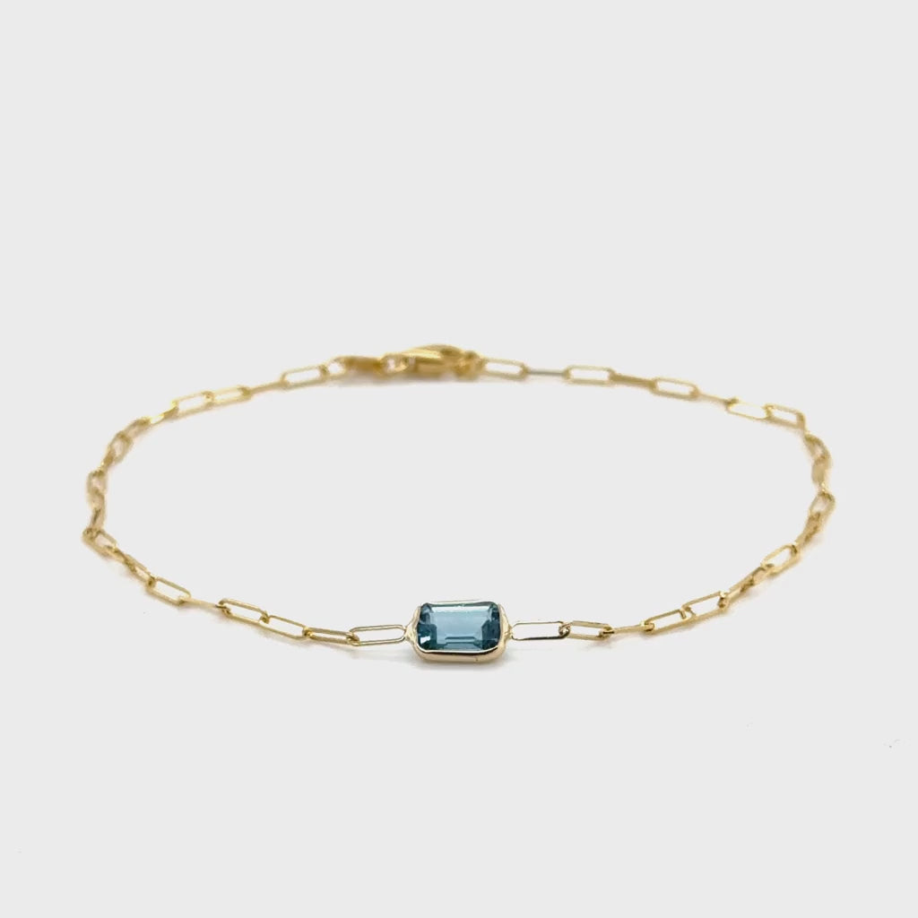 A dainty 14K gold paperclip bracelet featuring a baguette-cut Blue Topaz centerpiece, the December birthstone symbolizing honesty and clarity. This elegant and minimalist design is durable, versatile, and comfortable for everyday wear, making it a meaningful gift for birthdays, anniversaries, or milestone celebrations.