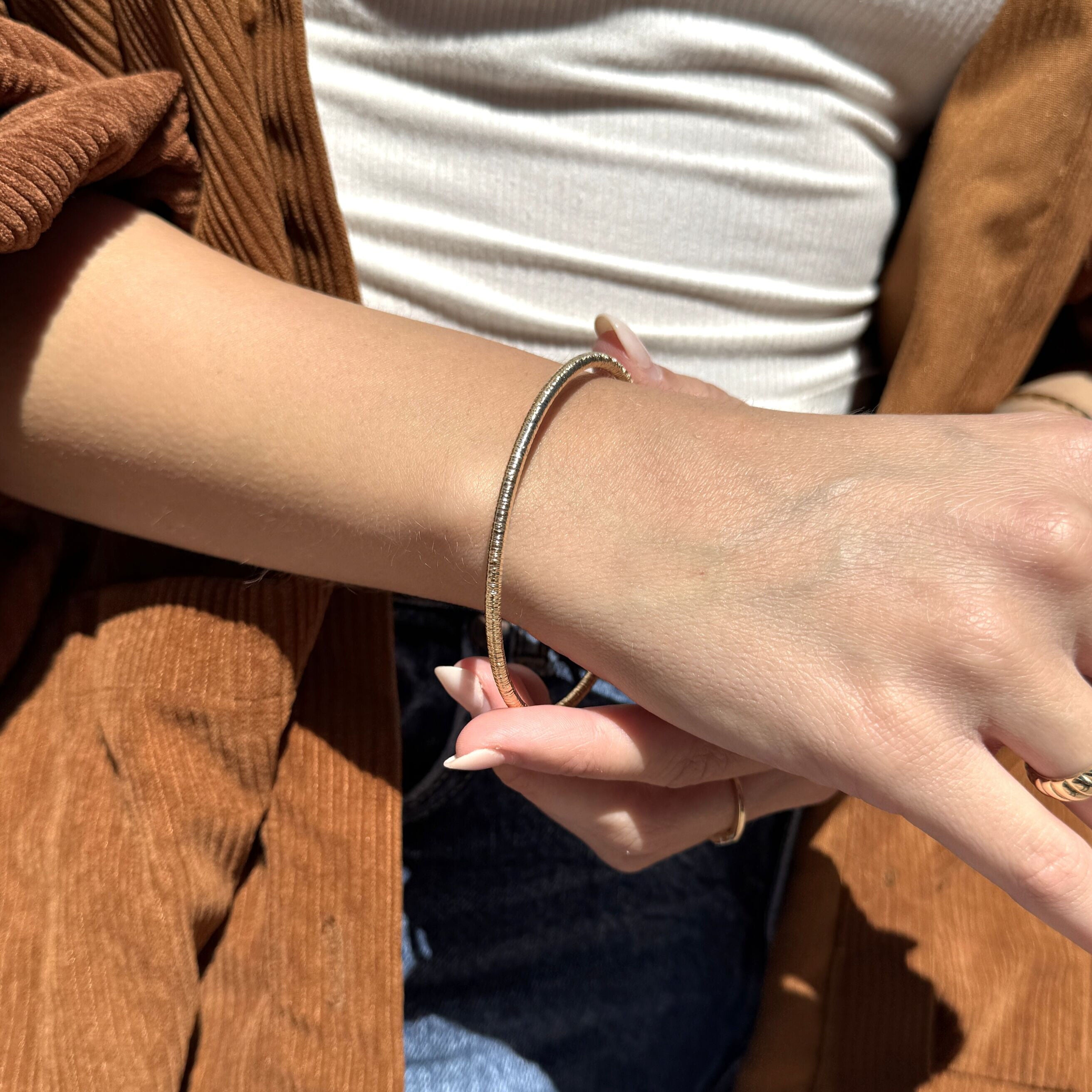 Slim 14K Gold Bangle paired with a white ribbed top and corduroy outer layer, creating a modern effortless vibe, making it a lovely gift for birthdays or casual occasions.