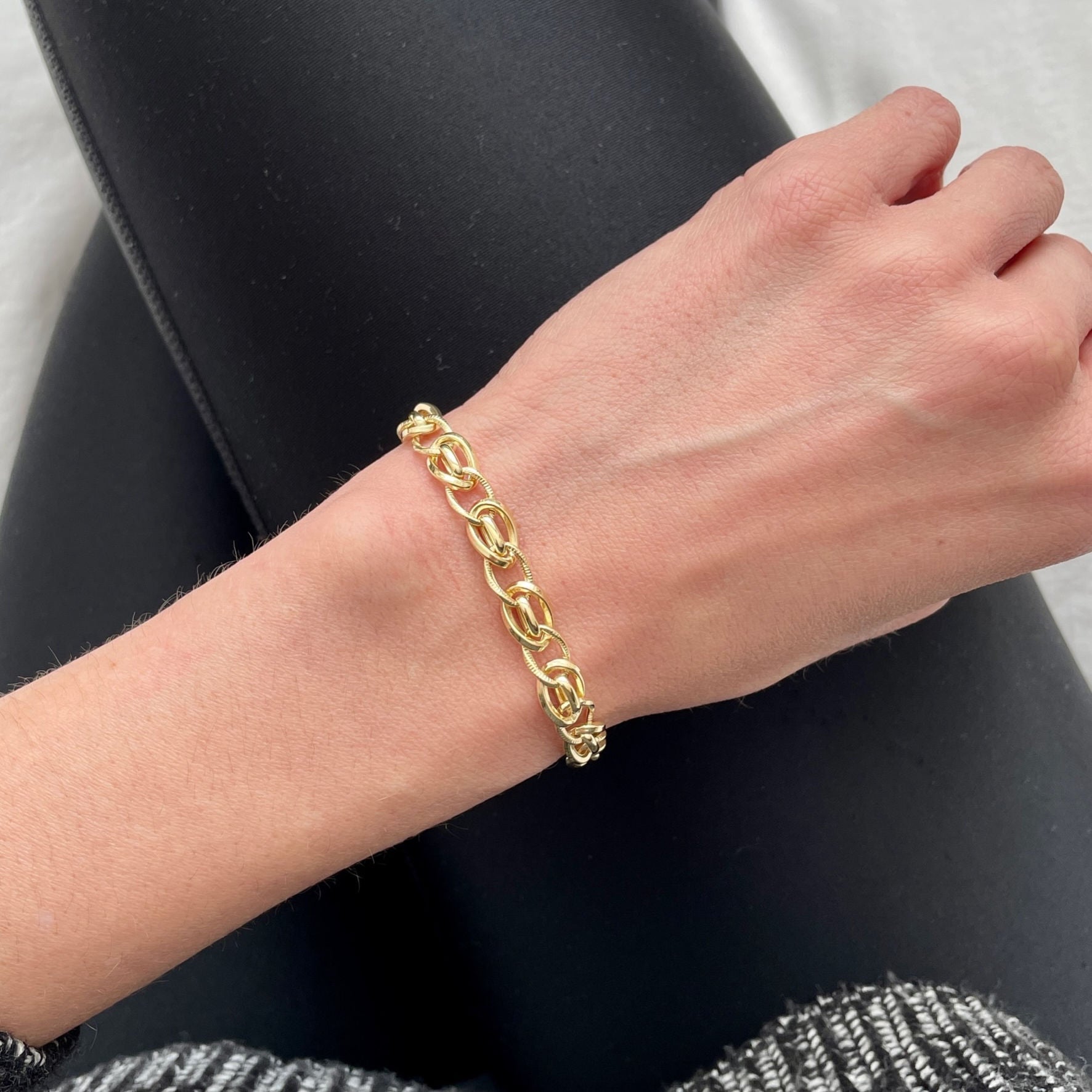 14K gold twisted oval link bracelet worn on the wrist with a casual black outfit. The bold gold links add timeless elegance and confidence to a minimal look. Perfect for everyday wear, casual meetings, or workdays where subtle luxury stands out.