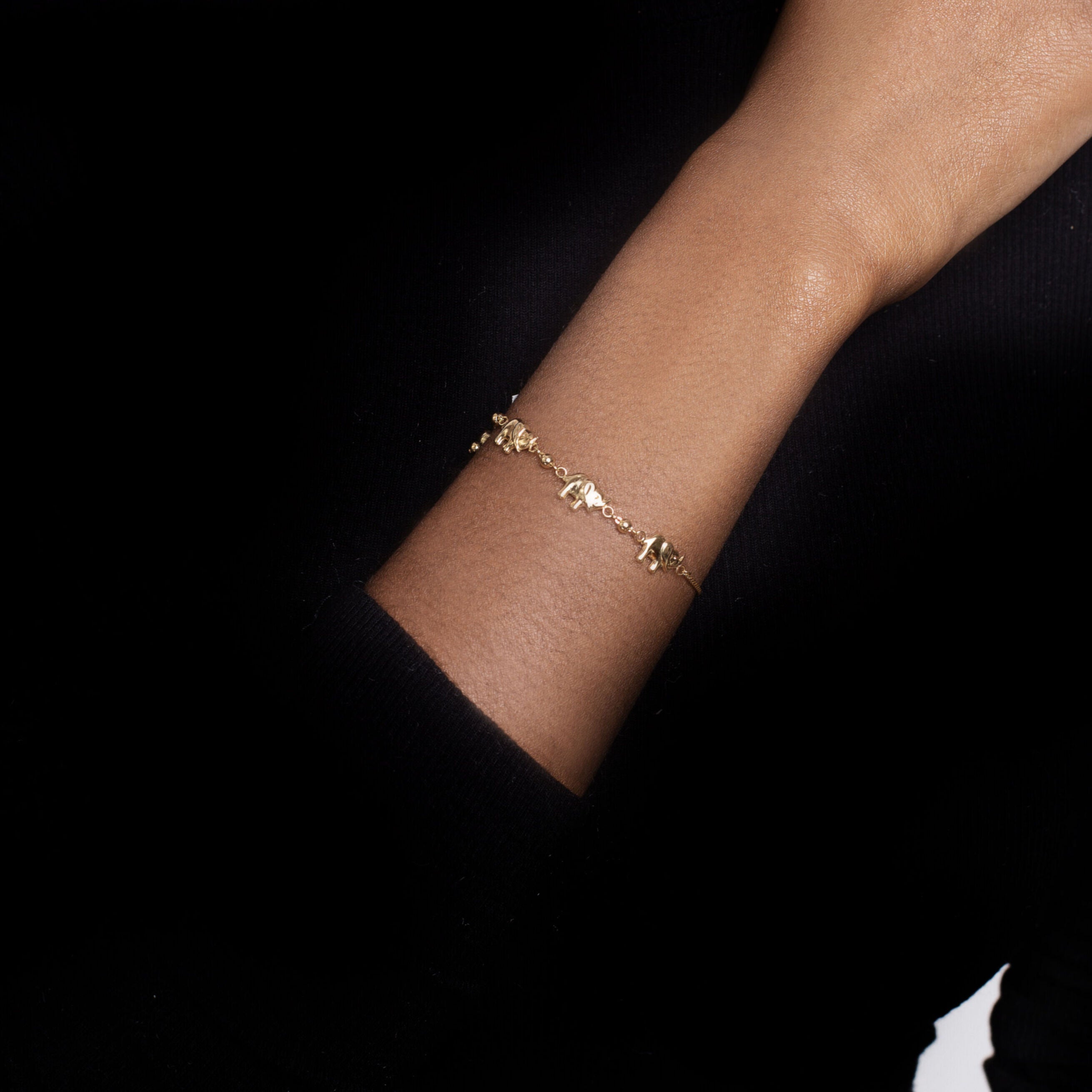 14K solid gold elephant charm friendship bracelet worn on the right wrist with a sleek black turtleneck. The dainty gold design enhances the minimalist outfit with elegance and confidence, perfect for workdays, casual meetings, or evening gatherings.