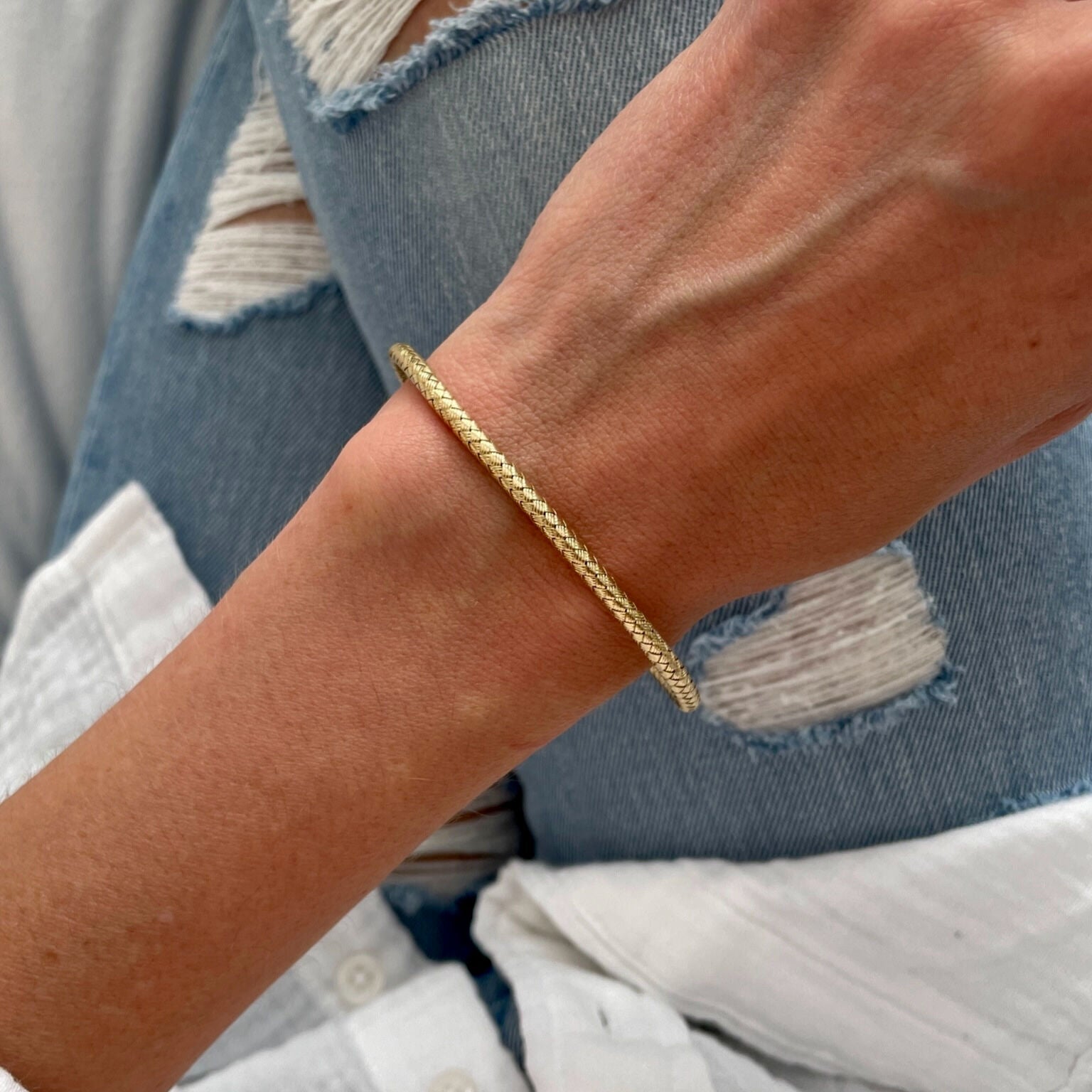 14K yellow gold woven bangle bracelet styled with a rolled shirt sleeve, adding polished sophistication to a relaxed outfit. Ideal for workdays or casual meetings.