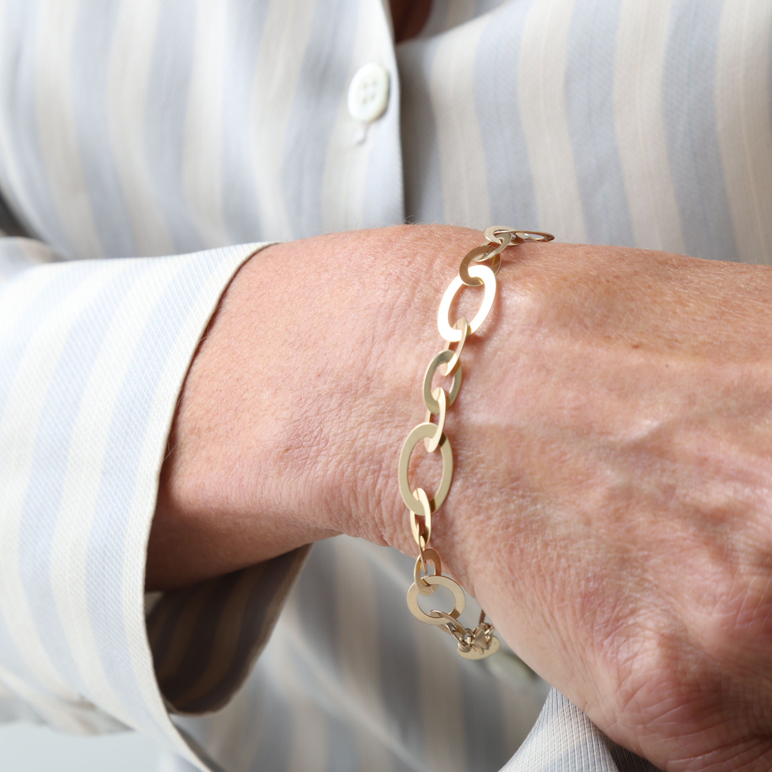 14K Yellow Gold Flat Oval Link Bracelet paired with a striped button-up blouse and coordinating gold necklace, ideal for work meetings or coffee dates