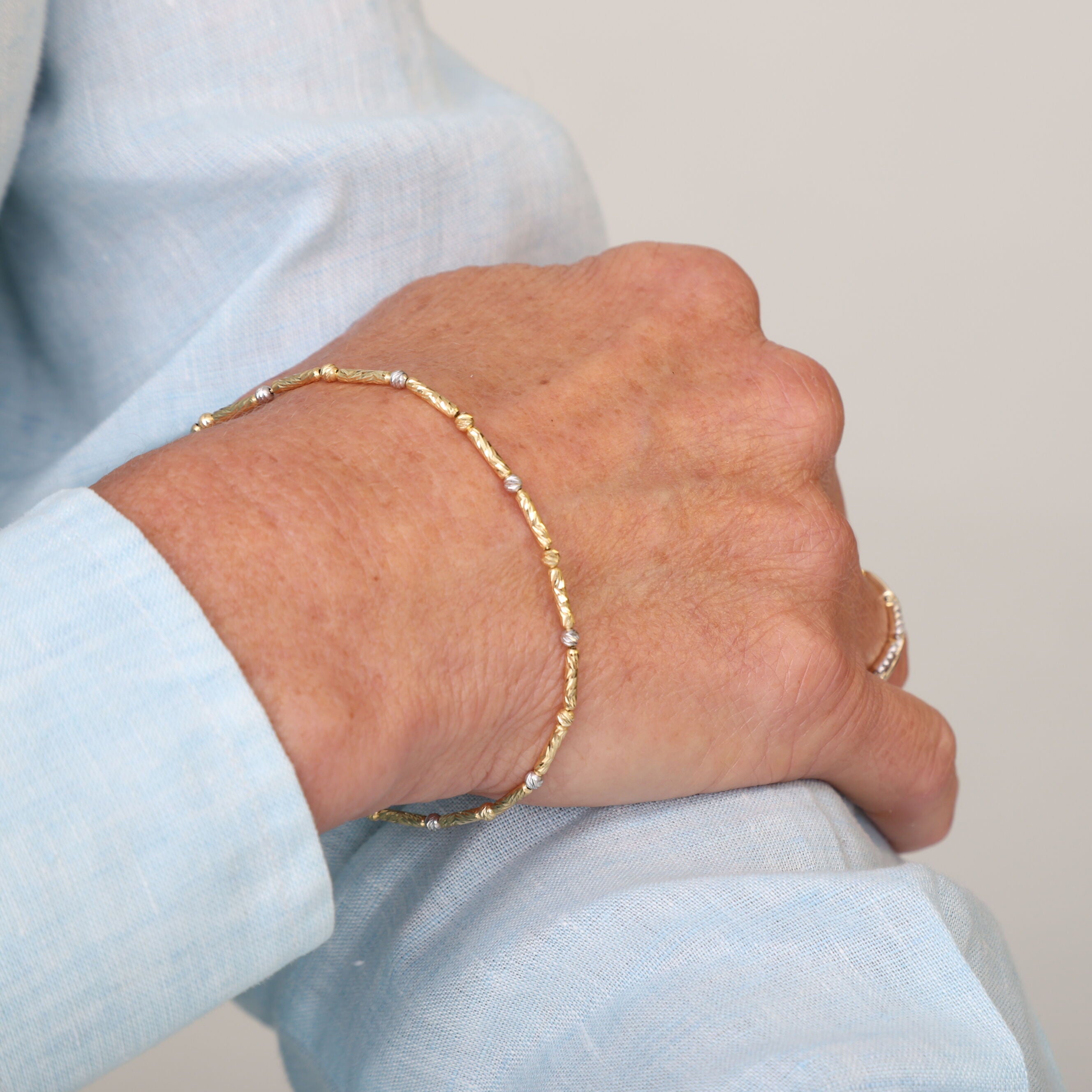 14K Two Tone Gold Bar and Bead Bracelet paired with a tailored blazer and gold ring, ideal for formal events or special evenings.