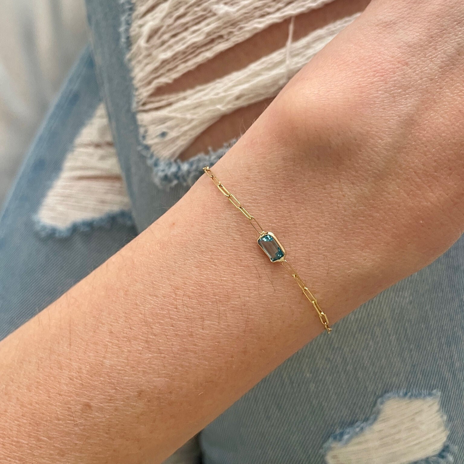 Dainty 14K gold Blue Topaz bracelet styled on the wrist with ripped denim jeans, adding a touch of elegance and sparkle to a relaxed outfit. Perfect for casual days, brunch dates, or everyday December birthstone style.