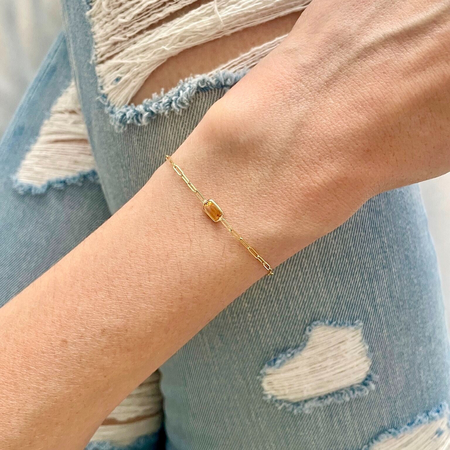 Dainty 14K gold bracelet with a natural Citrine gemstone, the November birthstone, styled on the wrist with distressed denim jeans. The real Citrine adds a warm glow that enhances a casual outfit, perfect for relaxed weekends or everyday prosperity-inspired style.