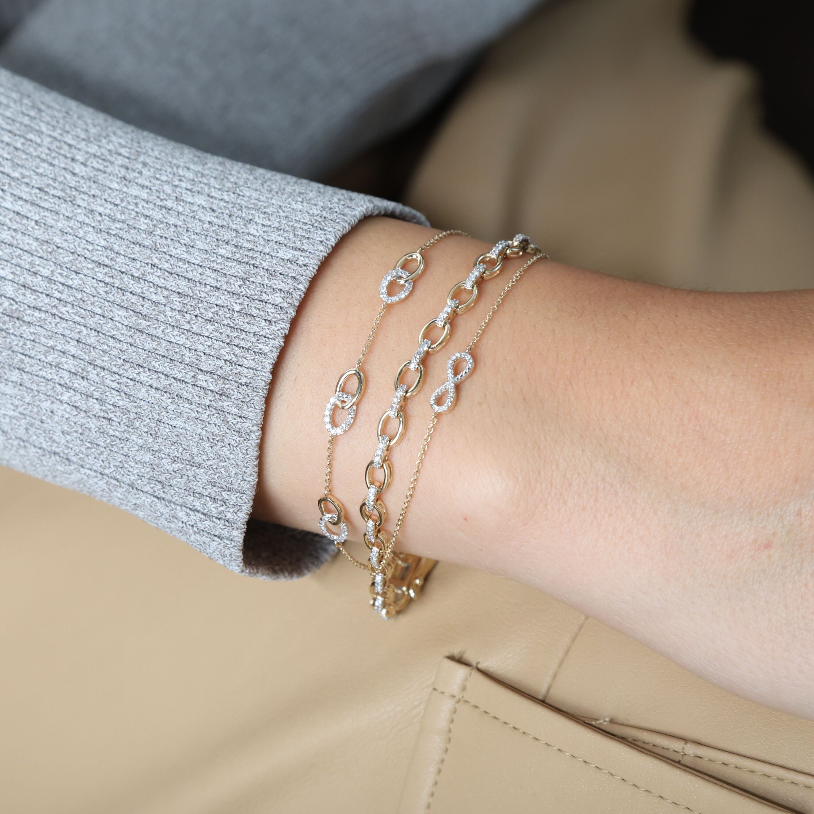 Diamond Oval Link Chain Bracelet in 14K Yellow Gold worn with slim diamond bracelets on a neutral beige outfit. The delicate diamond accents bring timeless elegance and sparkle, ideal for anniversaries, dinner parties, or refined day-to-night wear.
