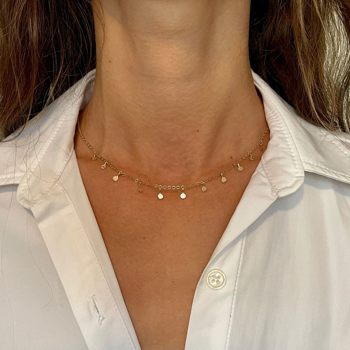 Model wearing a 14K yellow gold dangle disc choker necklace at the neckline with a white collared shirt.