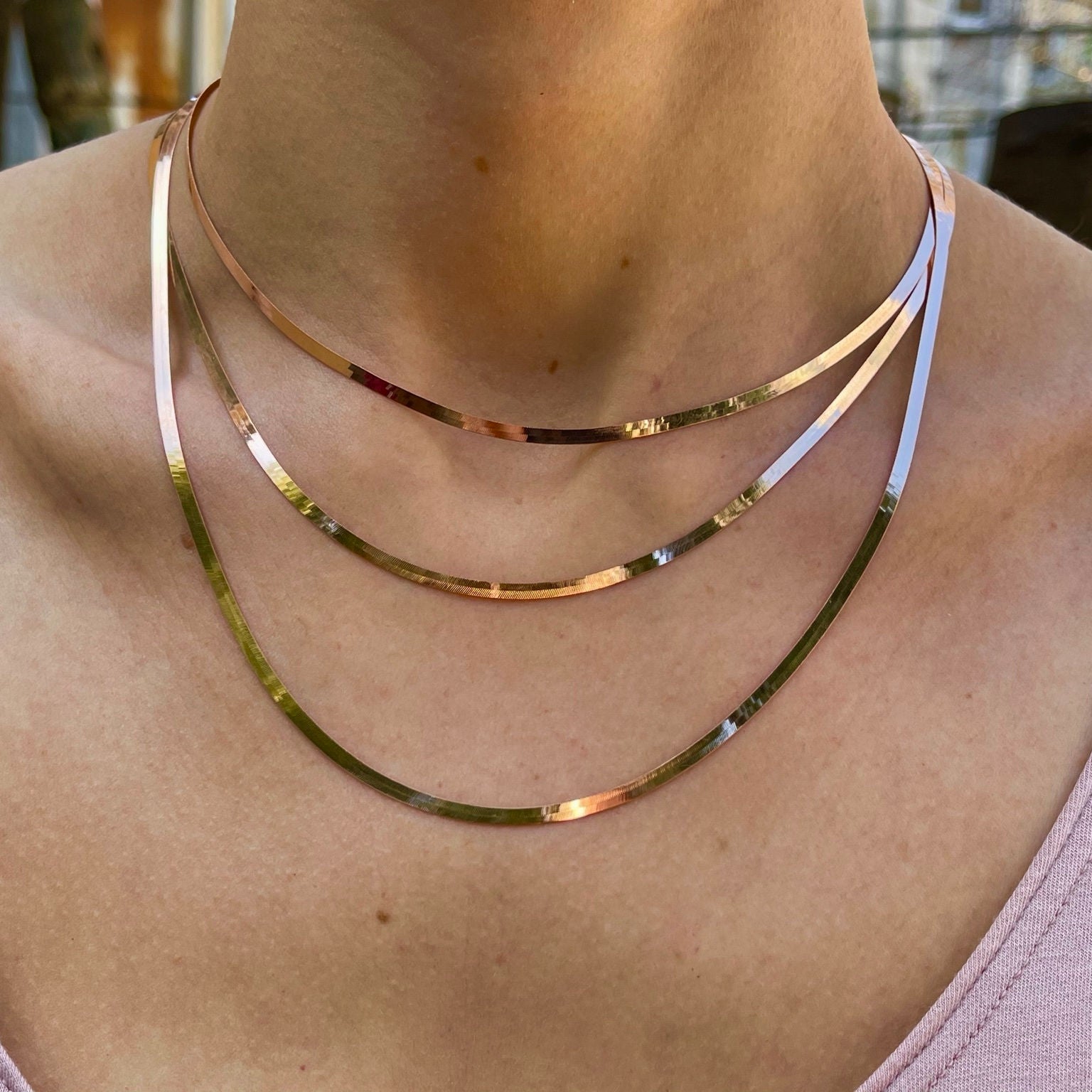 14K Solid Rose Gold Herringbone Necklace layered with delicate gold chains over a scoop neckline, creating a modern and sophisticated statement. The smooth flat design enhances elegance and balance, ideal for brunch dates, creative work environments, or elevated casual meetings.