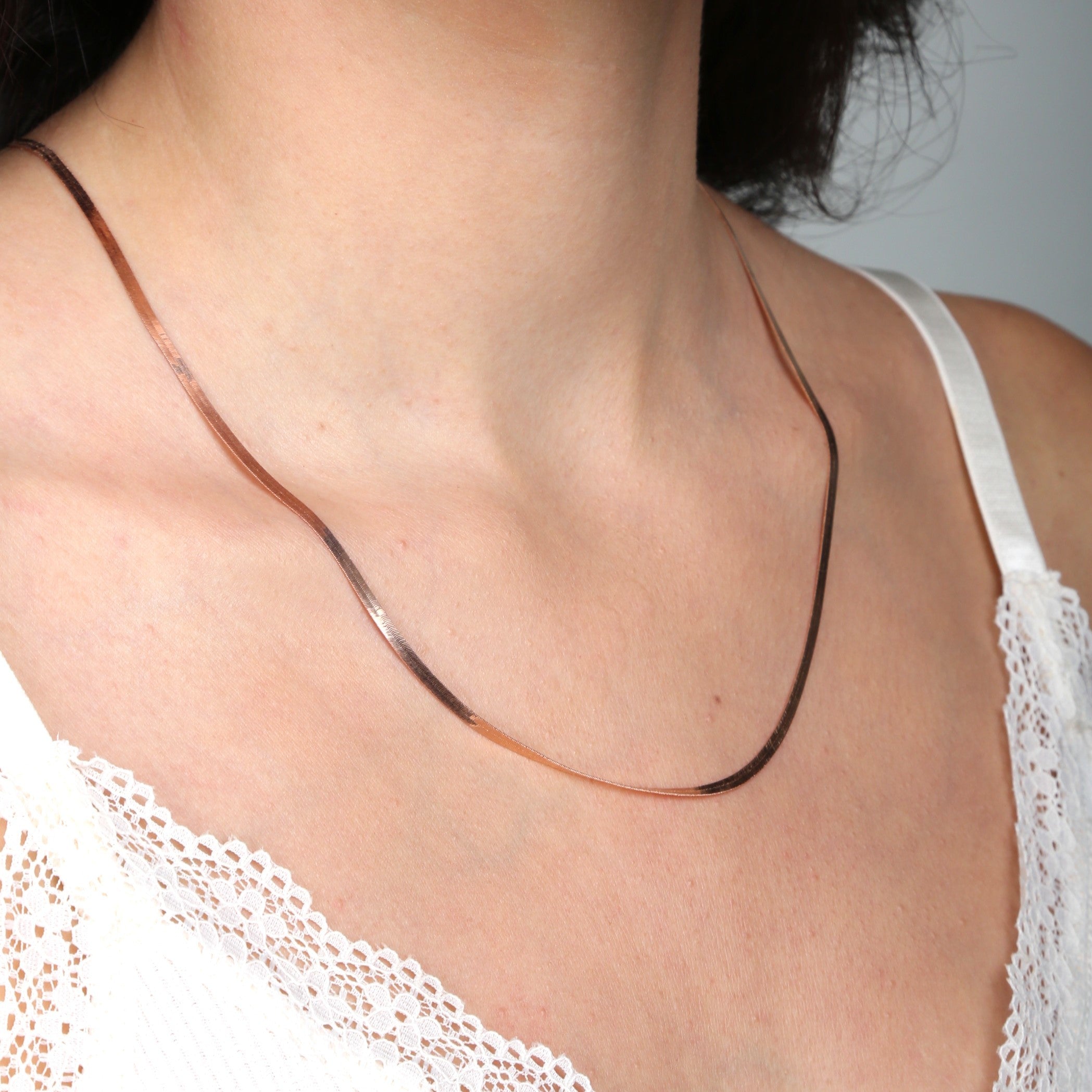 14K Solid Rose Gold Herringbone Necklace styled with a white lace neckline, resting flat against the collarbone for a soft and elegant everyday look. The polished flat chain adds refined confidence and timeless charm, perfect for casual outings, workdays, or relaxed daytime events.