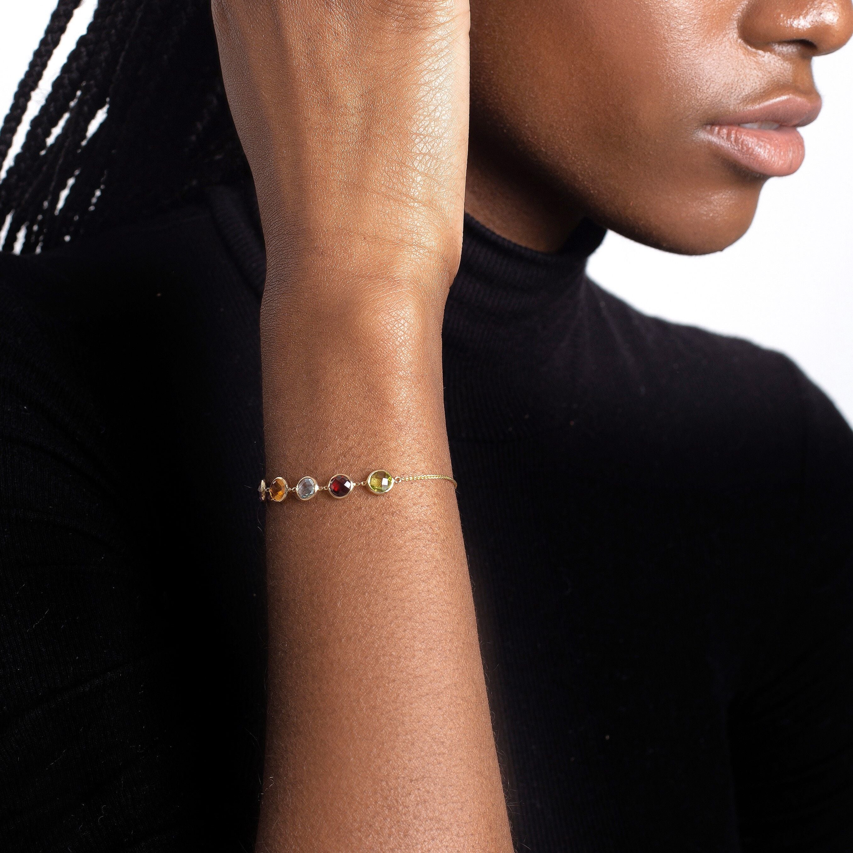 14K yellow gold friendship bracelet with Peridot, Garnet, Blue Topaz, Citrine, and Amethyst gemstones styled on a woman’s wrist with a black long-sleeve top. The colorful round gemstones create an elegant contrast against the dark outfit, adding confidence and timeless charm, ideal for everyday wear, casual meetings, or evening events.