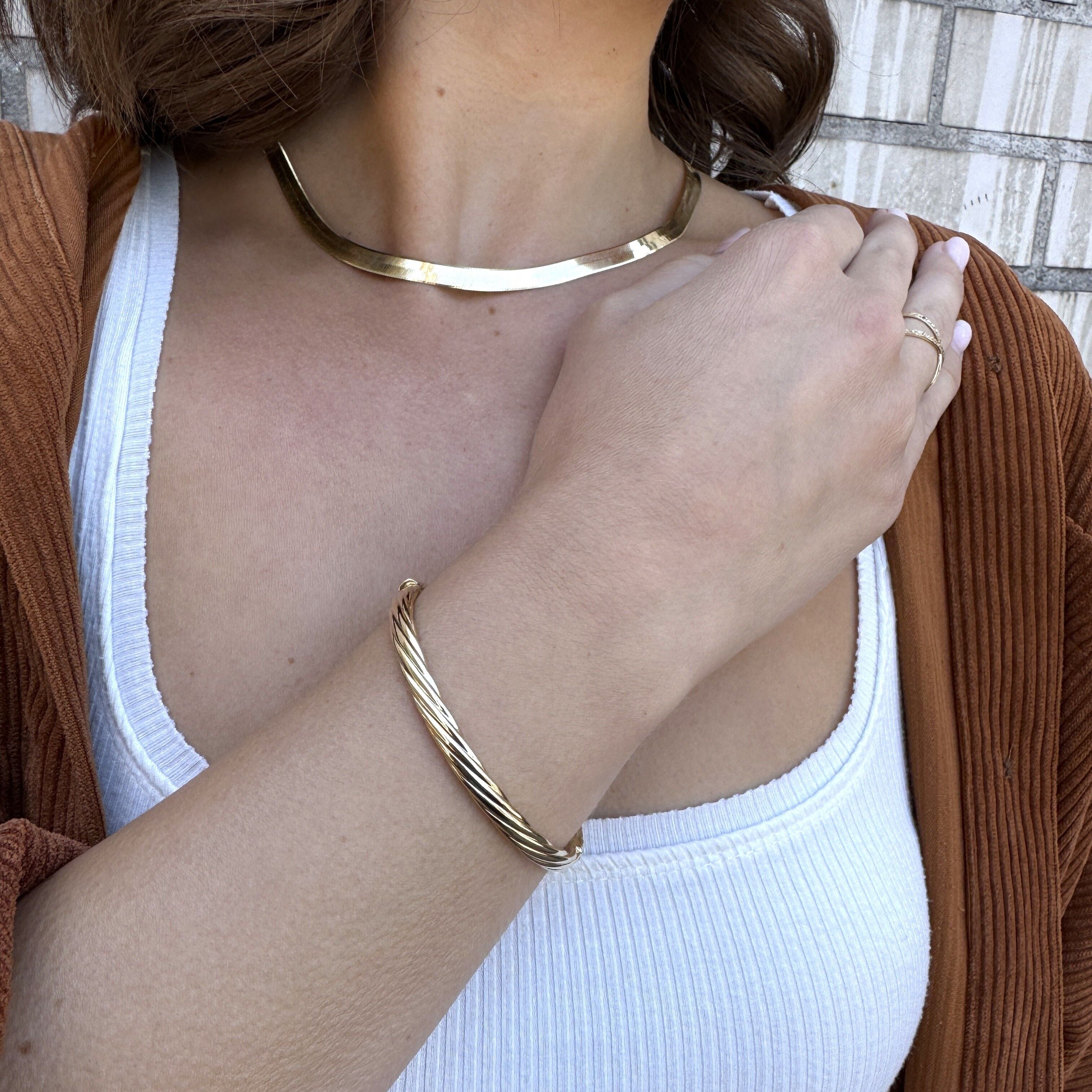 Woman wearing 14K gold twisted bangle bracelet, emphasizing its chic, solo-wear elegance on the wrist.
